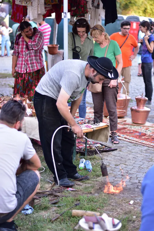 Meșter lucrând la un vas de cupru, cu vizitatori în jur