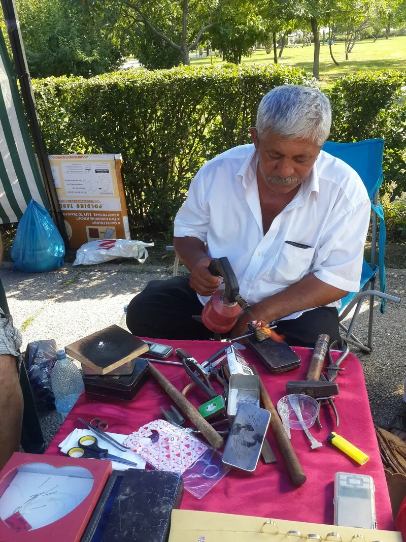Roma craftsman working at a table full of tools at an open-air fair