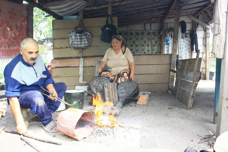 Roma coppersmith working a copper sheet over a fire, next to his wife