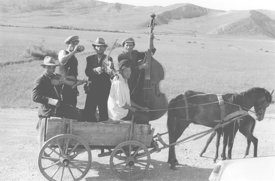 Black and white photograph: lăutari with violin and double bass on a horse-drawn cart